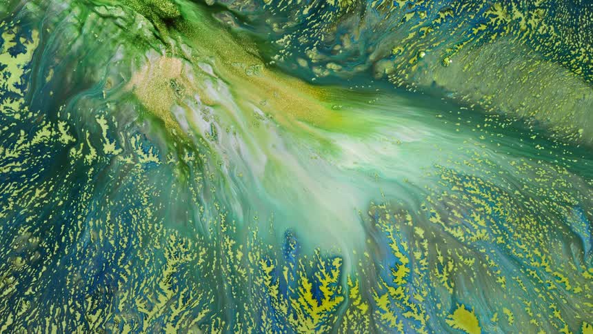 An abstract art project shows a shimmery blue and yellow base with an opening at the top which has green and white liquid pouring out of it