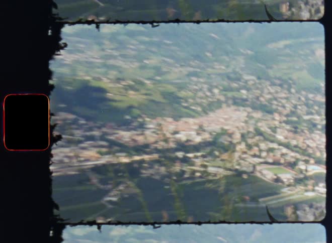 An aerial view of a city nestled amidst lush green vegetation with a majestic mountain range in the northern horizon