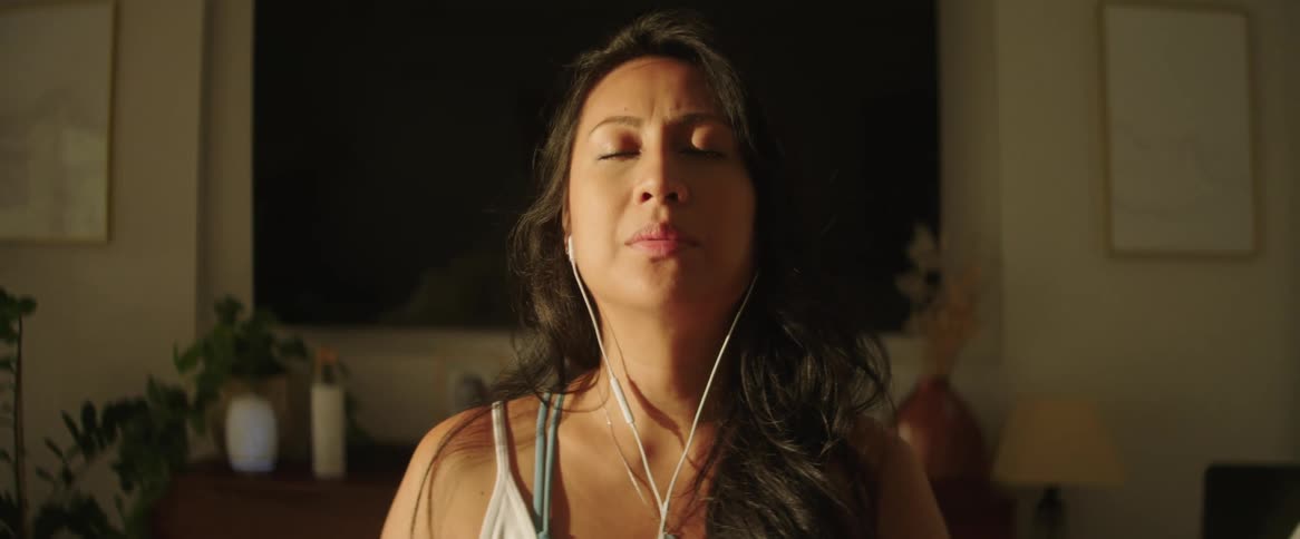 A close up of a woman wearing headphones with hear eyes closed breathing slowly in a room with lit shining in