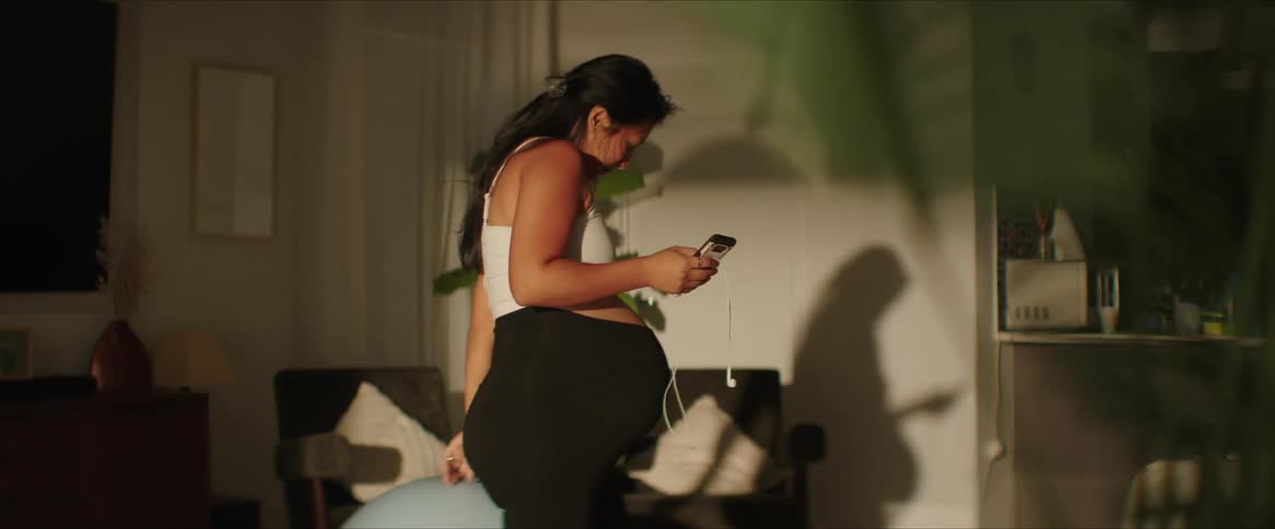 Woman with cell phone and headphones in her hands sitting on a pilates ball
