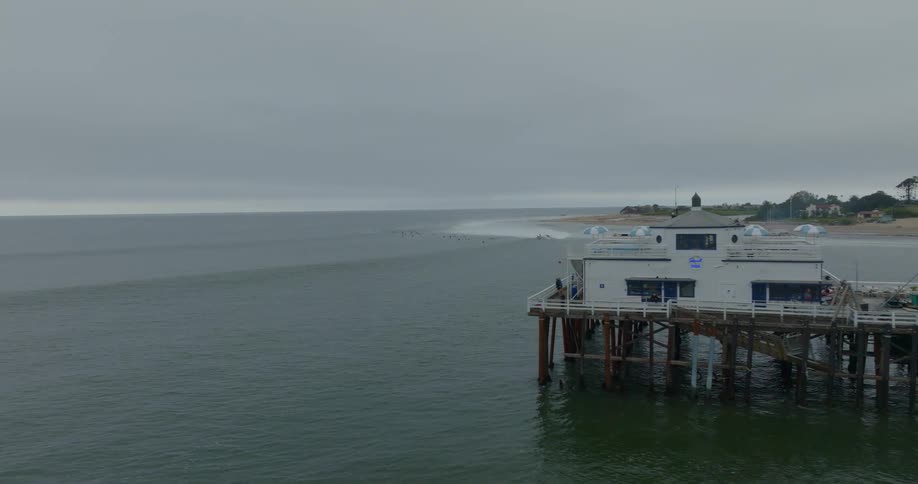 An aerial shot of Malibu pier revealing surfers surfing in the background