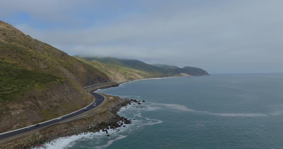 Cars drive along Pacific Coast Highway as waves roll in to shore