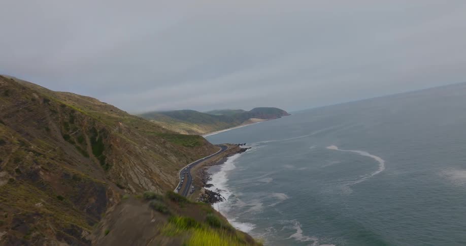 An aerial view of a road between tall rocky cliffs and the sea shore