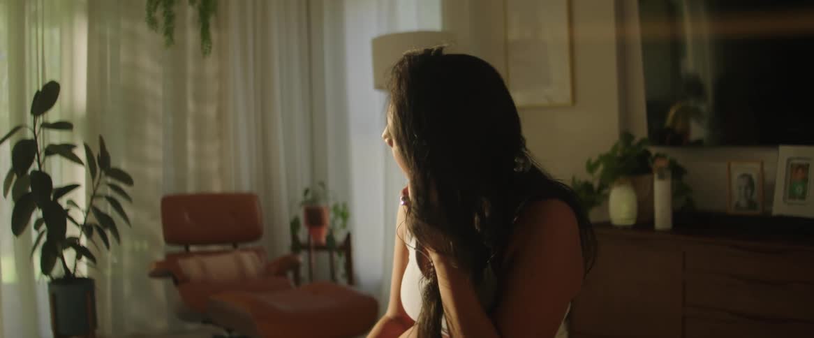 In the comfort of her own home a young lady sits with a serene expression wearing a wired earbud connected to her phone lost in the world of music she immerses herself in the melodies and lyrics that fill her ears