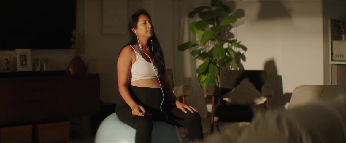 Pregnant woman sitting on a pilates ball checks her phone before doing yoga