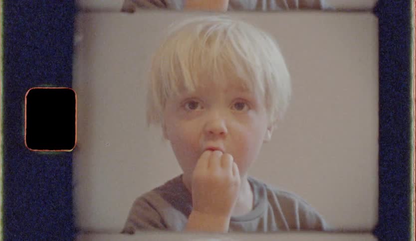 Child eating food at a wooden table with his baby brother by her side