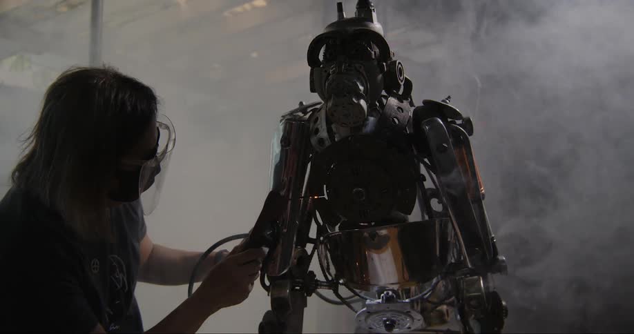 Man standing up on a factory welding metal parts to a robot