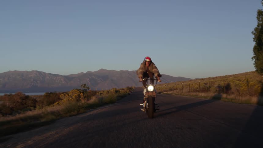 A motorcycle driver stands on the seat and lets go of the handlebars