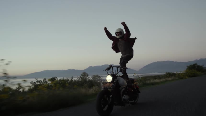 A man stands up on his moving motorcycle
