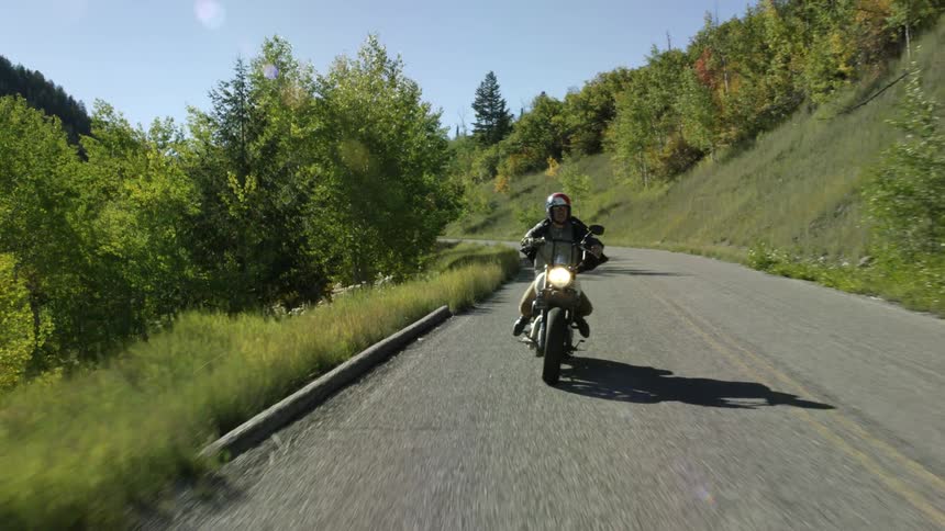 A person rides a motorcycle on a small road near a hill