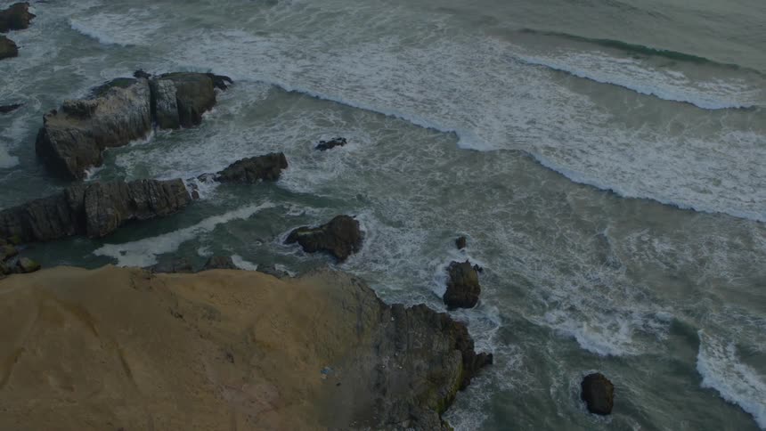 Ocean waves roll into a rocky coastline in the evening