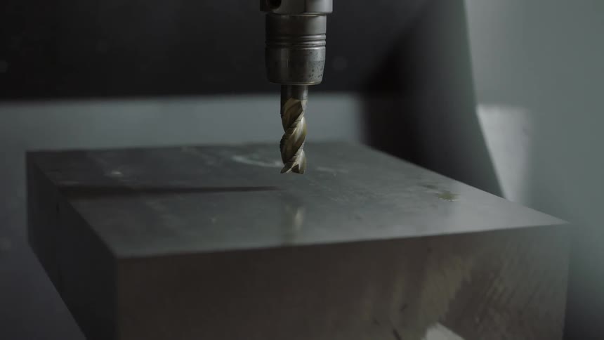 A drill bit mounted in a device hovers idly just above a metal block