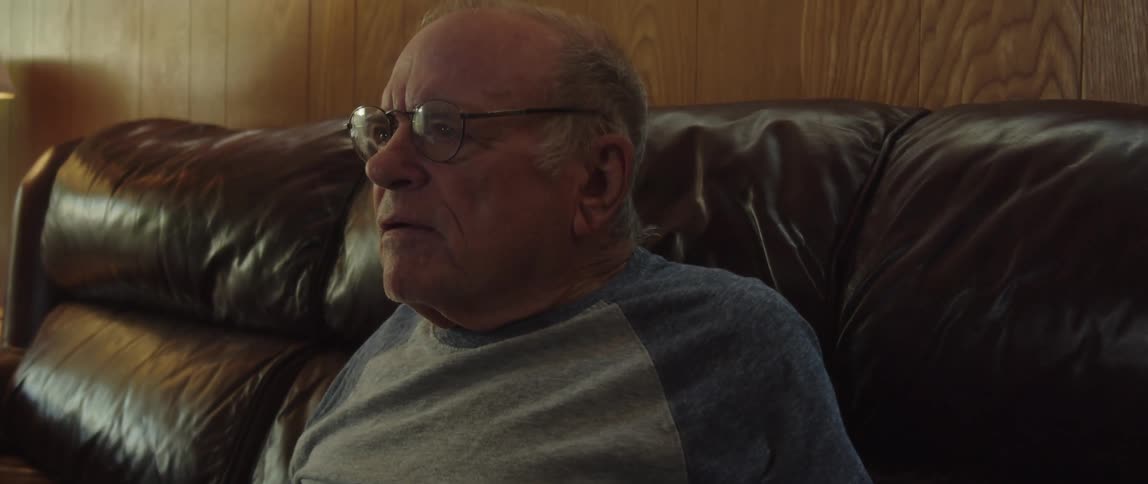 A man watches tv and gets momentarily excited at what he sees while sitting on a couch