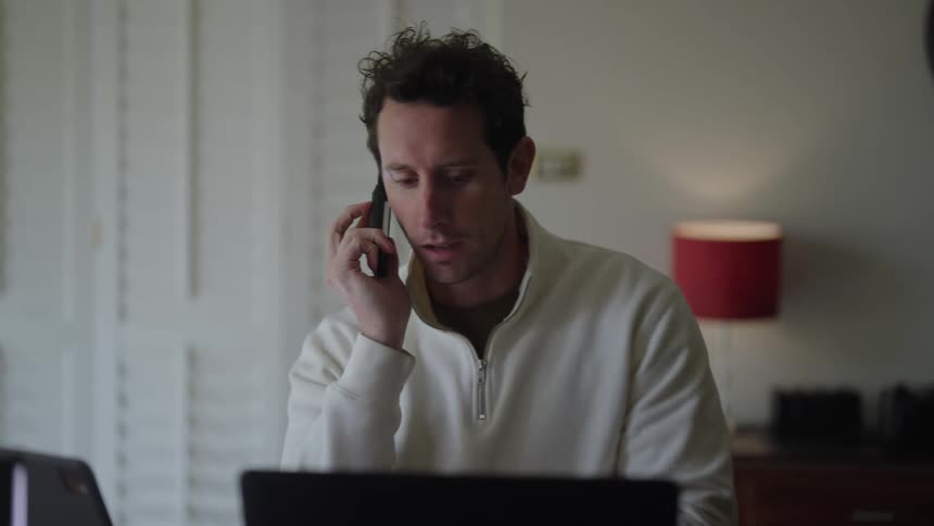 Busy man at his home desk multitasking by talking on the phone and simultaneously working on his laptop