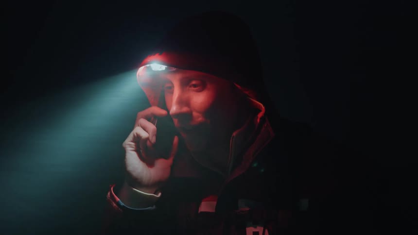 A man wearing a headlamp talks on his phone at night and in the rain