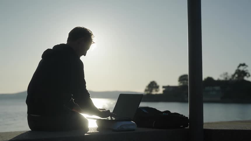 A man is typing on his keyboard by the water
