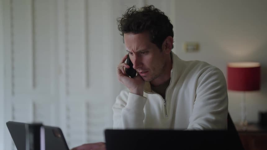 A man talks on his cell phone while he is reviewing information on his tablet computer