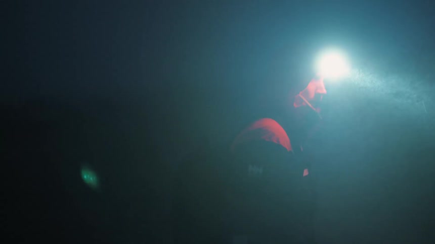 A man wearing a headlamp and raincoat walks outdoors at night