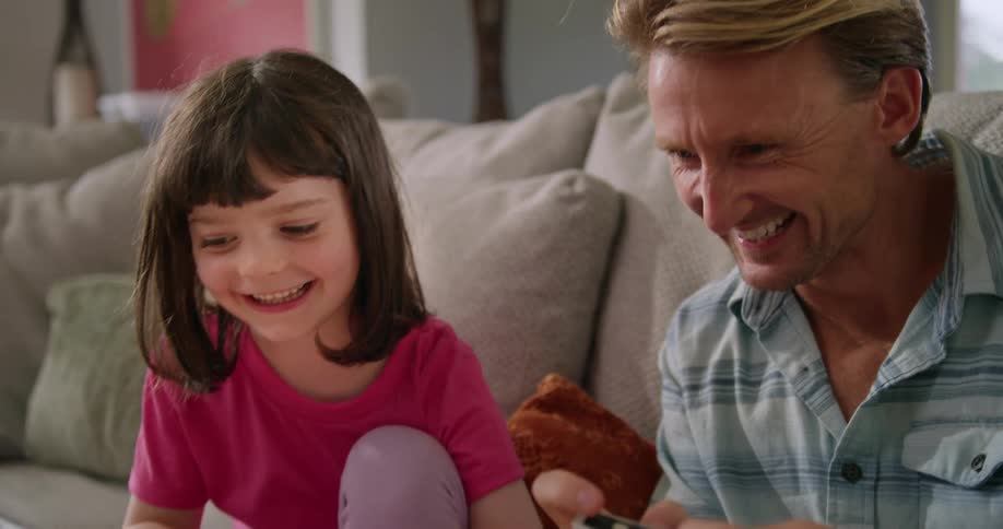 A man plays a video game with a little girl in the living room of a house