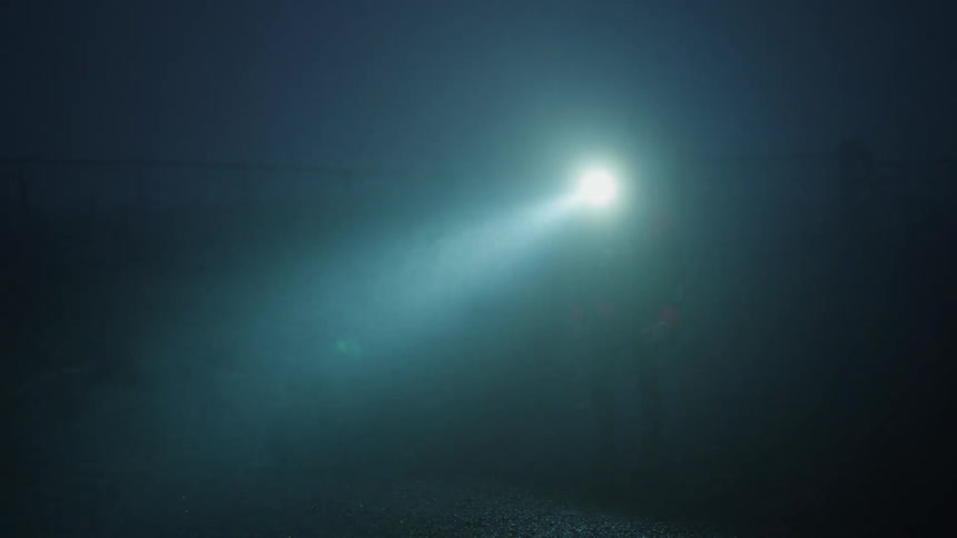 A man is walking on a road in the foggy darkness wearing a bright headlamp flashlight