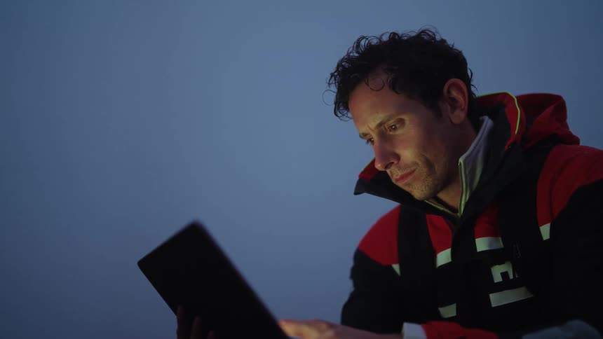 A man holds a tablet computer while he is wearing a jacket outdoors