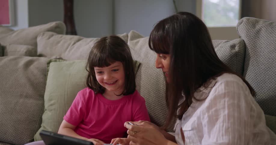 A woman plays a video game with a little girl while they sit together indoors