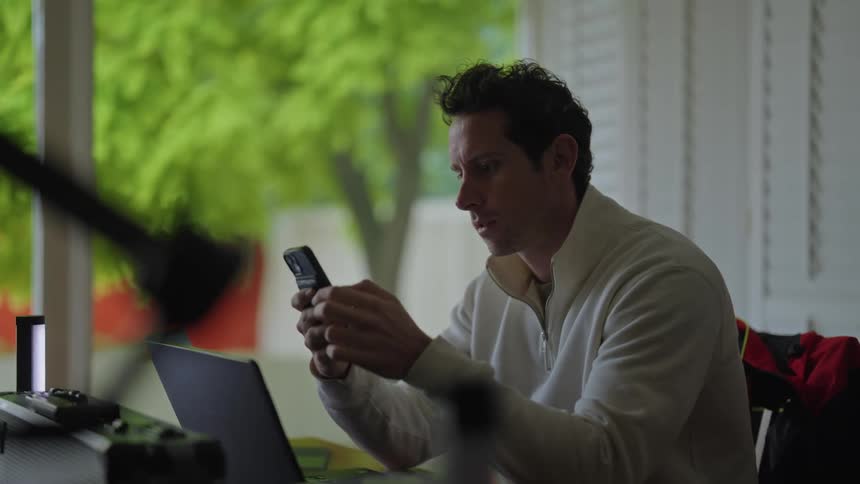 Man sitting at his desk in front of his laptops while typing on his smartphone