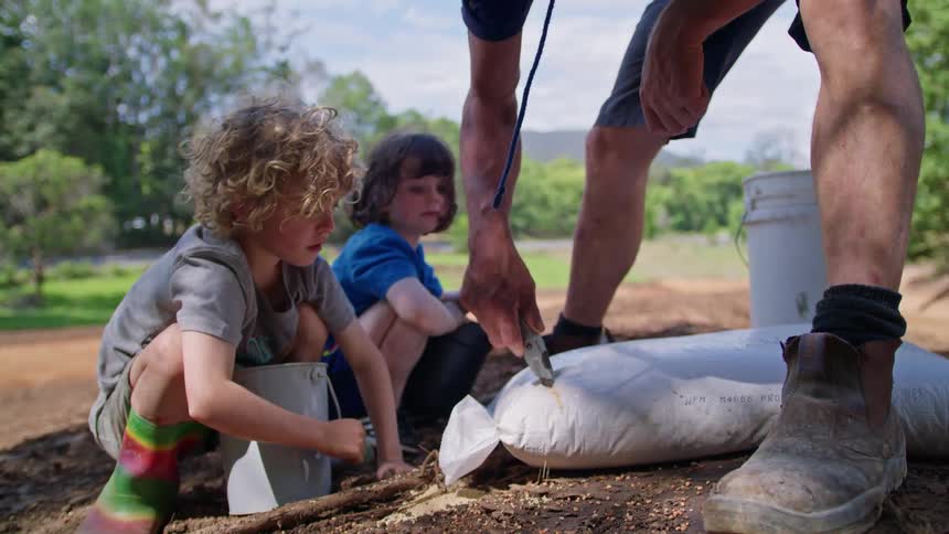 Children watch a man cut a bag of seeds open