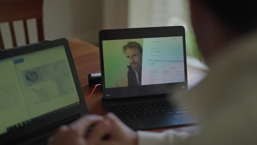 Man with two notebooks on his work desk having a video call meeting on one of them