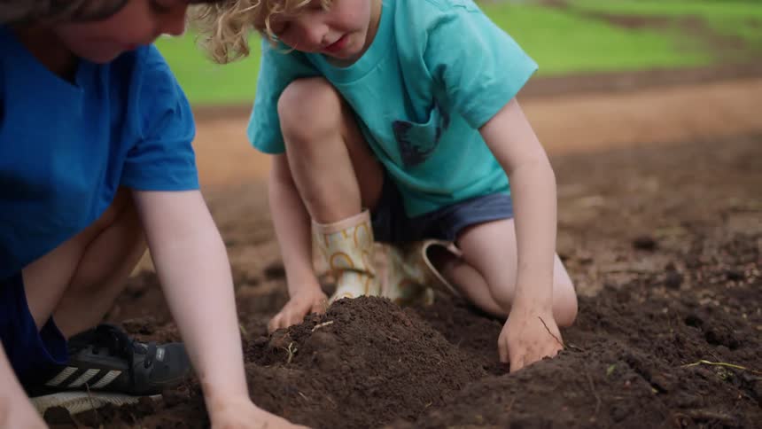A pair of children play in the dirt outdoors during the day