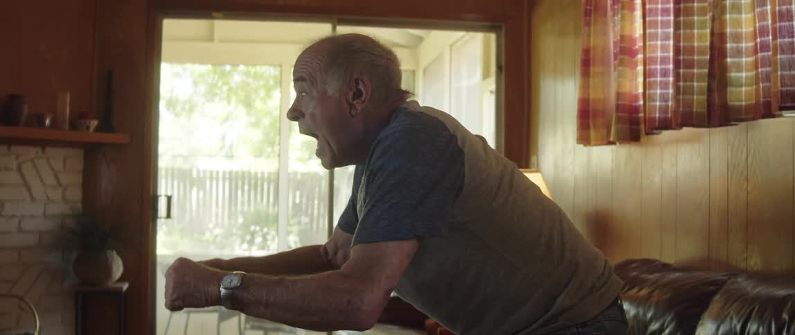 A man watching sports on tv in the living room standing up from the couch as he celebrates