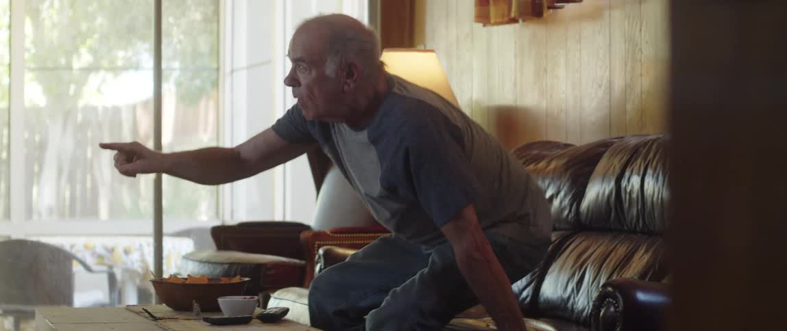 An elderly man standing up from a couch pointing his finger with excitement
