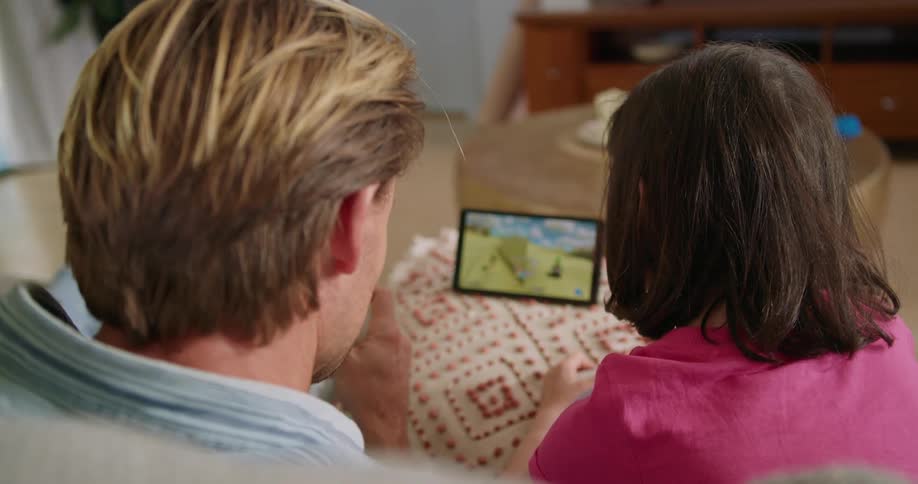 A man and a little girl play a video game together while sitting side by side indoors during the day