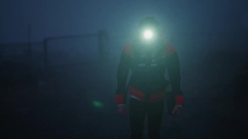 A man wearing a headlamp and jacket walks through the rain