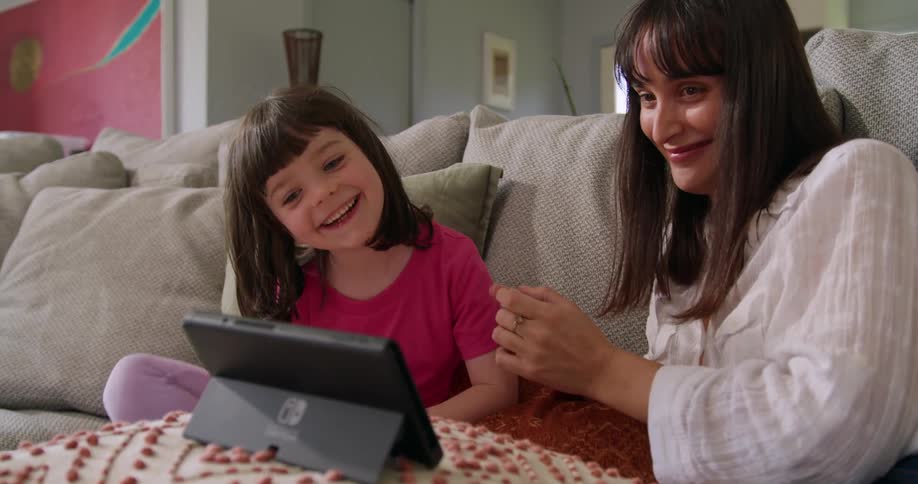 A woman plays a video game with a little girl in the living room of a house