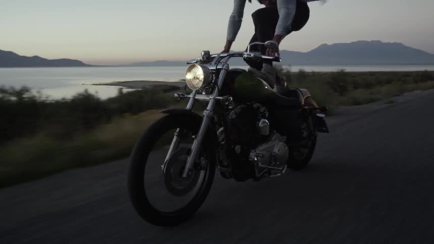 A man is standing on a motorcycle riding down a small road
