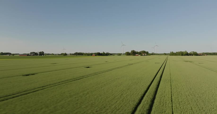 Wind turbines spin on rural farmland land under a clear blue sky