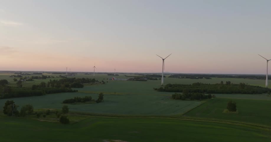 Wind turbines spin in fields in the countryside at sunset