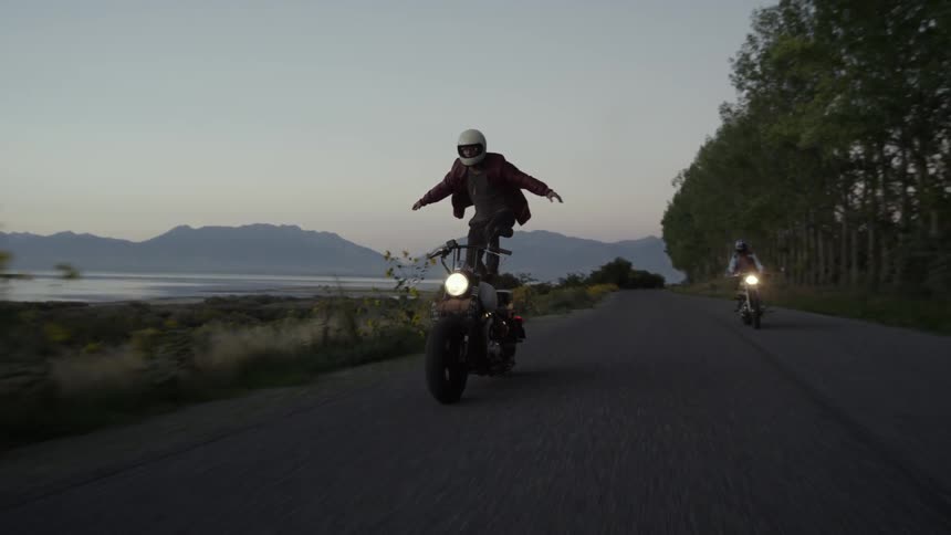 A man riding a motorcycle is standing holding his arms out