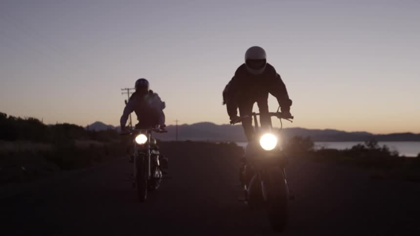 Two people race down a road at dawn standing on motorcycles