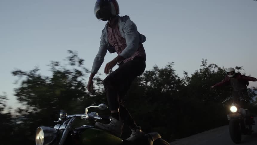 Two men balance on motorcycles in a rural area