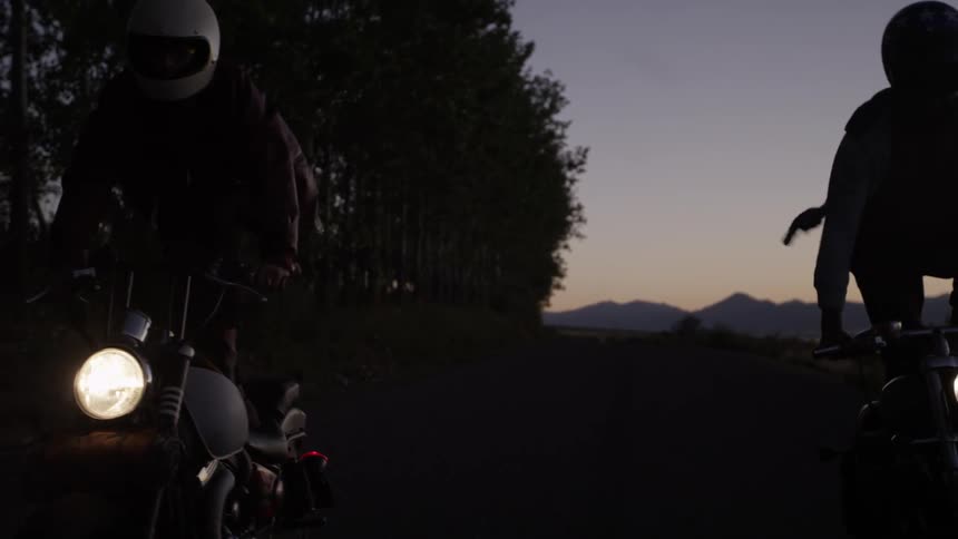 Two people do a trick standing as they ride motorcycles