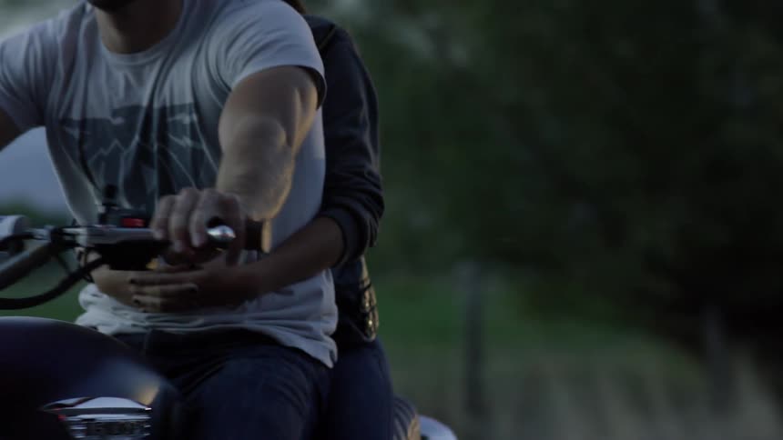 A man rides a motorcycle with a woman behind