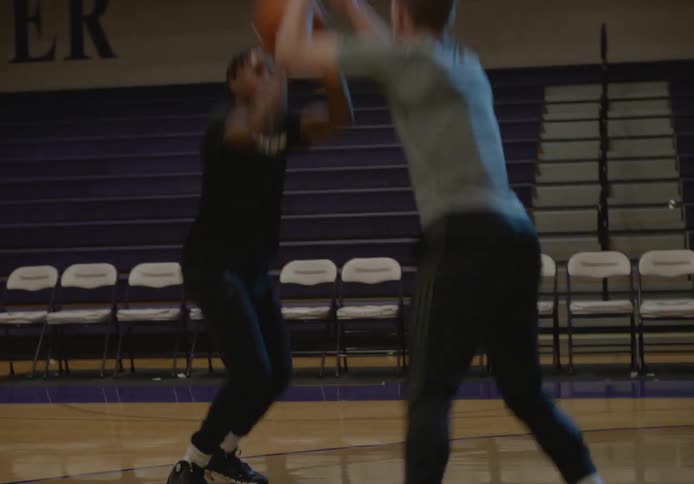Friends playing basketball on a university basketball court with one of them scoring a basket