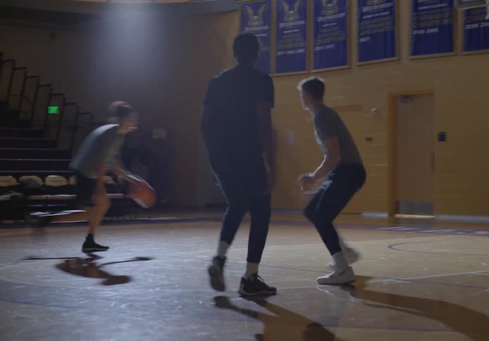 Three young men practice playing basketball in a gymnasium