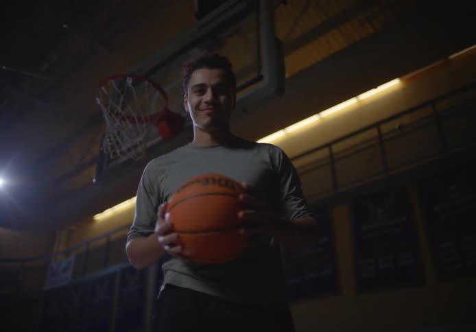 A man smiles while holding a basketball