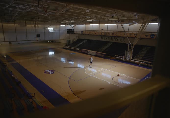 Young man in an empty basketball court practicing basketball attempting to improve his shots