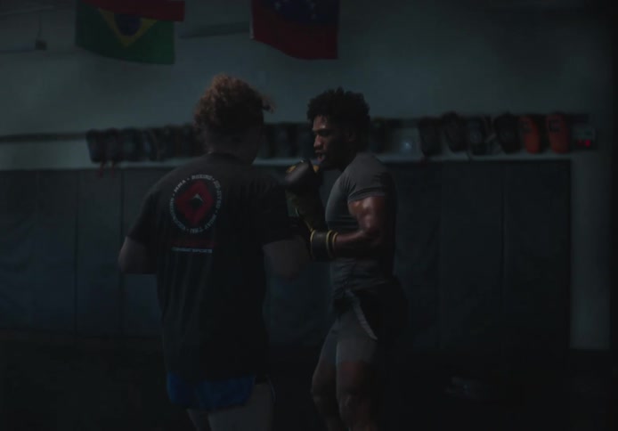A man wearing boxing gloves practices with another person holding pads