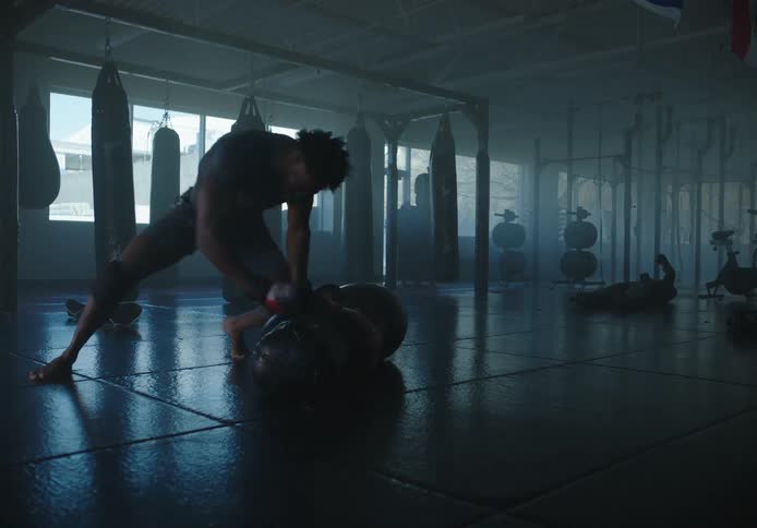 Man wearing boxing gloves aggressively punching a boxing bag on the floor of an empty gym