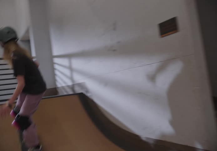 Girl wearing a safety helmet and knee pads practicing skateboarding in an indoor skate park